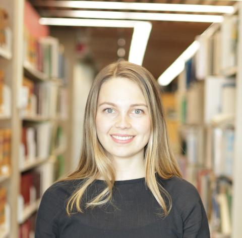 A person is standing in front of an aisle of books.